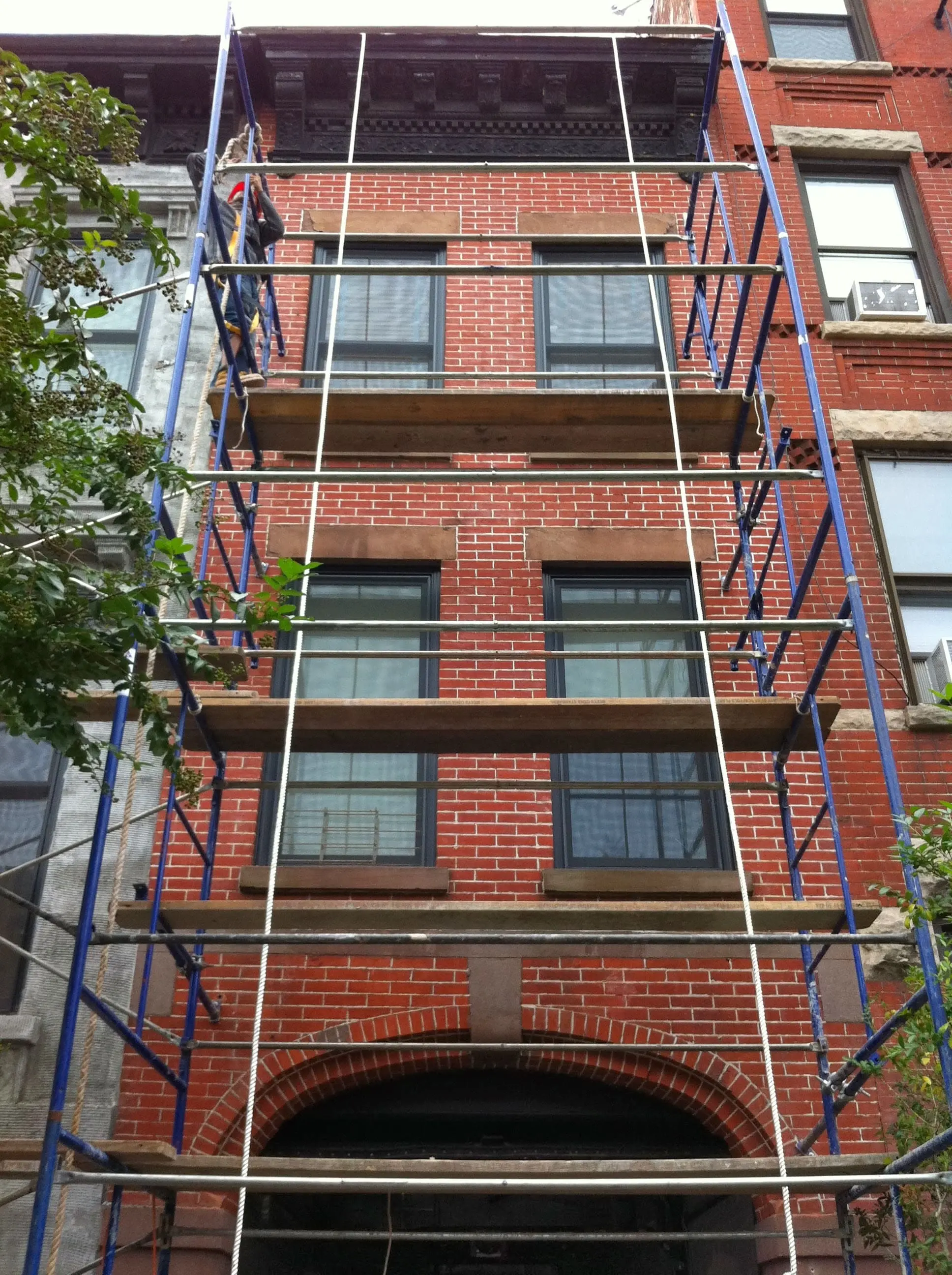 Expert masons laying and repointing brick joints on an NYC brownstone facade